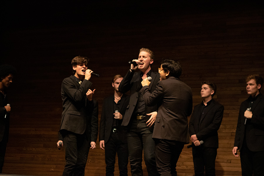 William Schmid and other Melodores stand on stage holding microphones and singing